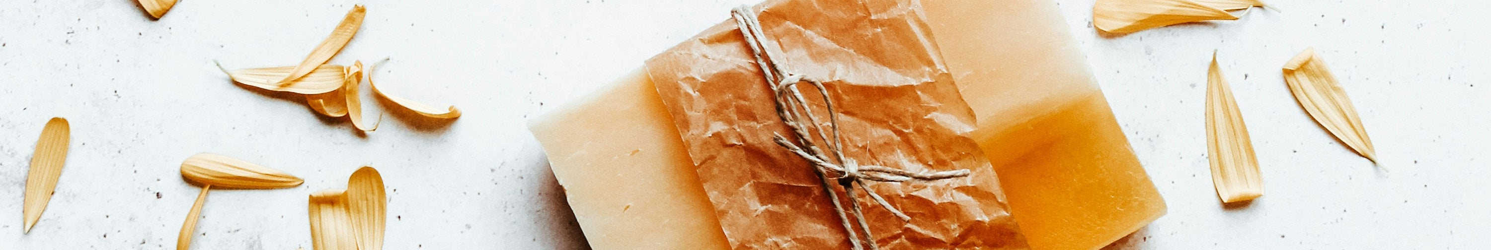 Bar of soap with a natural texture on a light surface with scattered yellow petals.